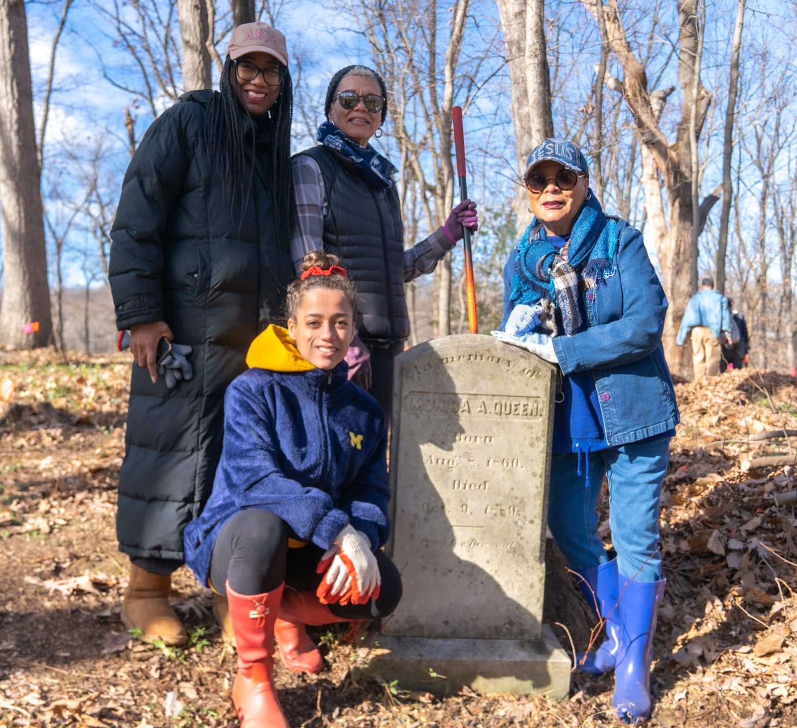 From left to right, Julie Ennis, sisters Dr. Stephanie Locke and Dr. Veronica Bryant are joined in front by Julie Ennis' daughter McKenzie Ennis, at the gravesite of their ancestor, Monica A. Queen, in the cemetery at Sacred Heart Parish in Bowie, Maryland. On Jan. 16, 2023 on the Martin Luther King Jr. holiday, the family members joined other volunteers in clearing brush and debris on a hillside near the cemetery where there may be hundreds of unmarked graves, possibly including the burial sites of enslaved people who worked on a Jesuit plantation in that area in the 1700s and 1800s. The Catholic Standard’s articles on the Sacred Heart Cemetery’s gravesites received an honorable mention award for best coverage of racial inequities in the 2024 Catholic Media Awards competition of the Catholic Media Association. (Catholic Standard photo/Mihoko Owada)
