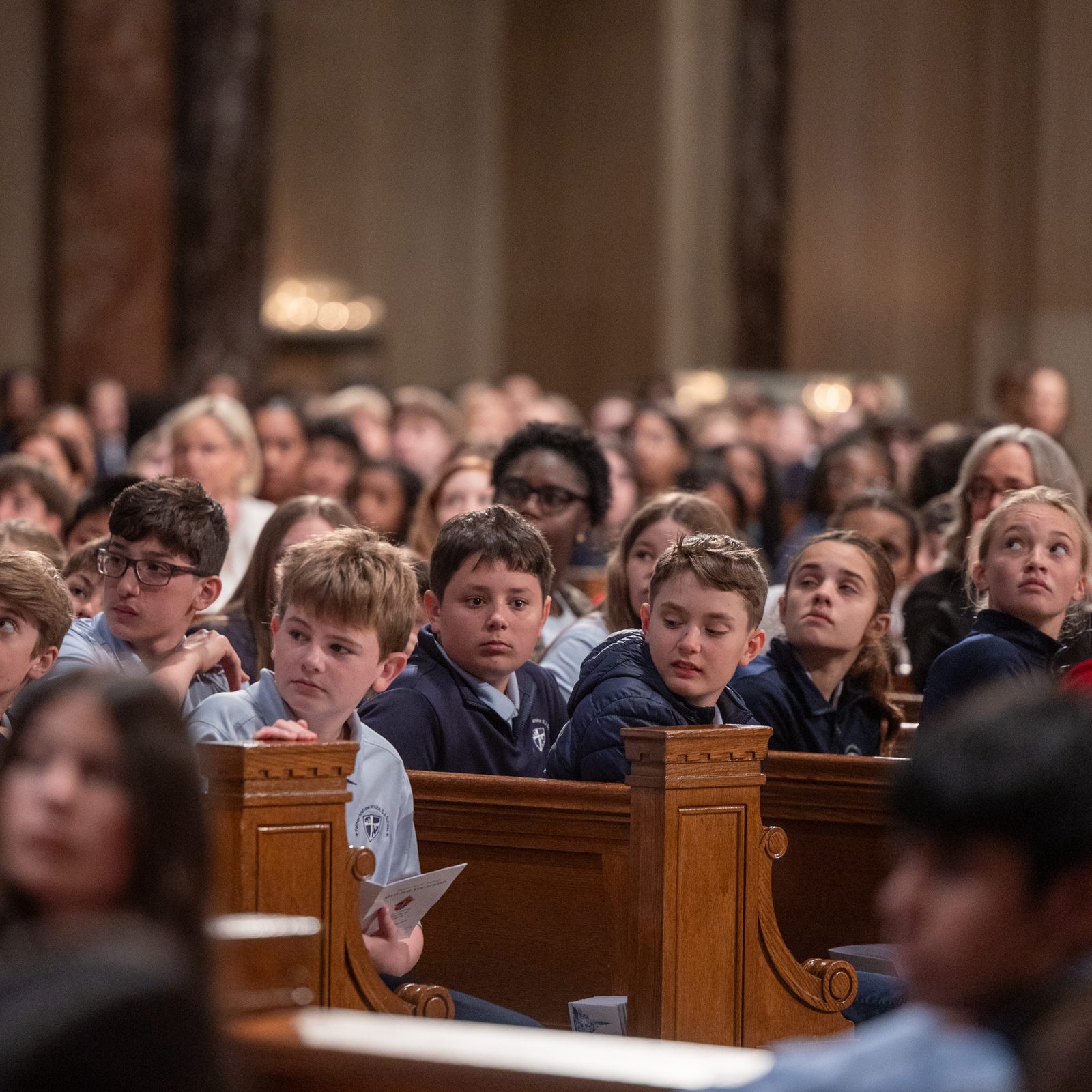 Students look toward the marble bas relief titled “The Universal Call to Holiness” in the National Shrine’s Great Upper Church as Father Brendan Glasgow invites them to reflect on the Church’s teaching that everyone is called to be a saint. (Catholic Standard photo by Mihoko Owada)