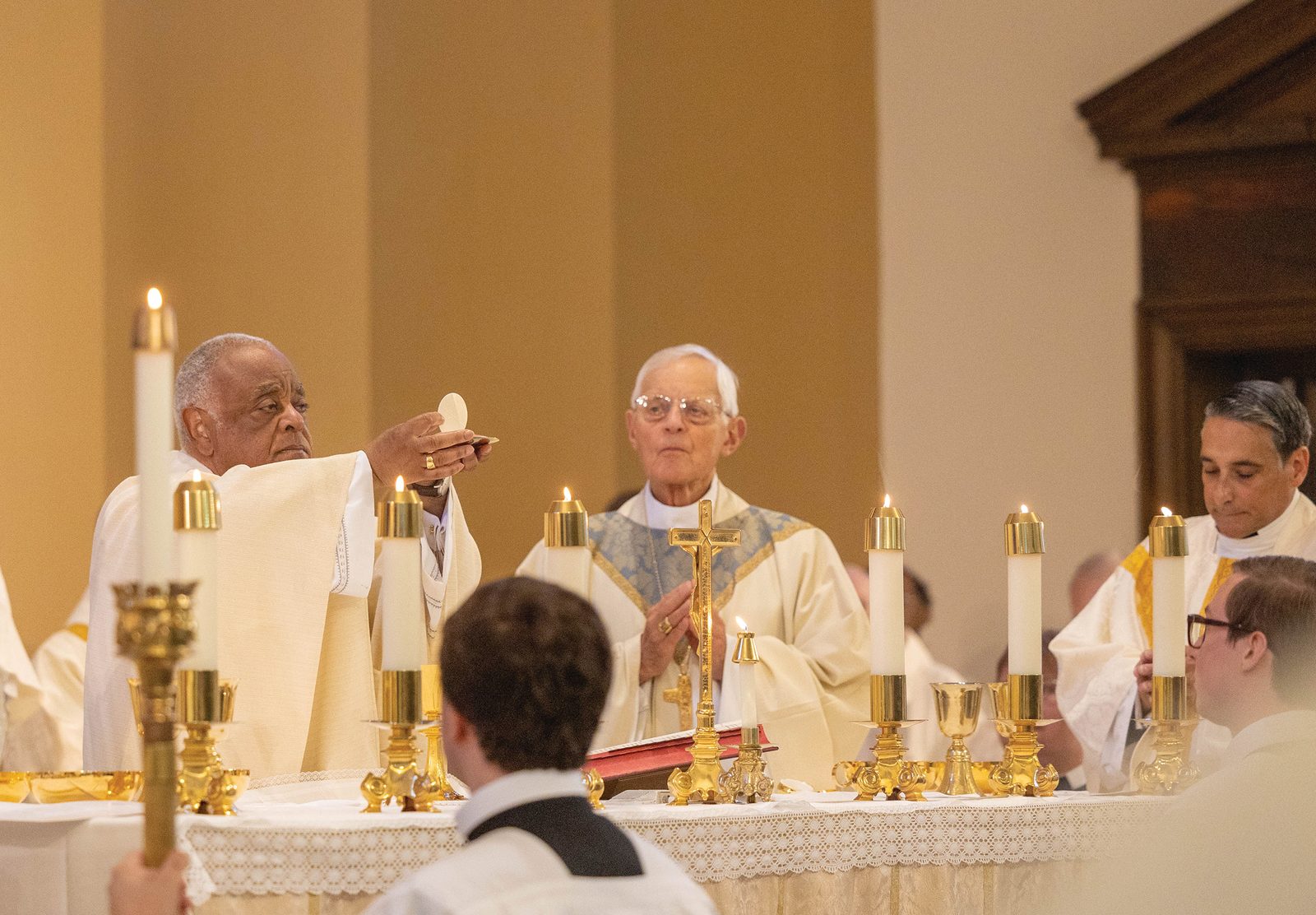 During July 10 Pontifical Mass of Thanksgiving for the Canonical Erection of the Washington Oratory, Cardinal Wilton Gregory, archbishop of Washington, elevates the sacred host. To the right of Cardinal Gregory is Cardinal Donald Wuerl, archbishop emeritus of Washington who in 2013 established the community-in-formation of the Oratory in The Roman Archdiocese of Washington. At far right is Father Richard Mullins, pastor of St. Thomas Apostle Parish. (CS Photo by Mihoko Owada)