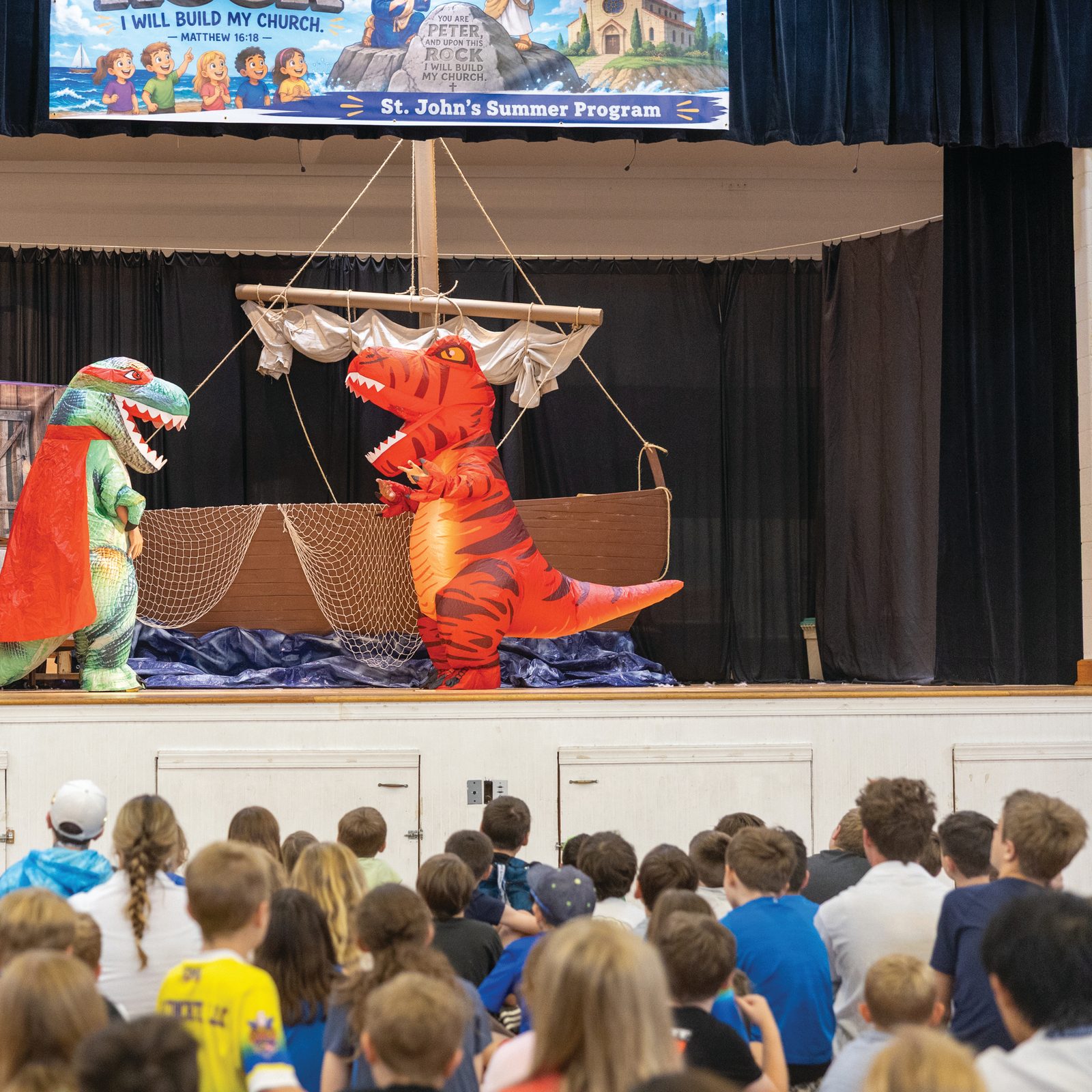 Counselors in inflatable dinosaur costumes perform during the morning show on July 21 at St. John’s Summer Program at St. John Francis Regis Parish in Hollywood, Maryland, as campers watch from the gym floor. The daily show combines songs, skits, jokes and costumes before children head to their individual camps. (Catholic Standard photo by Mihoko Owada)