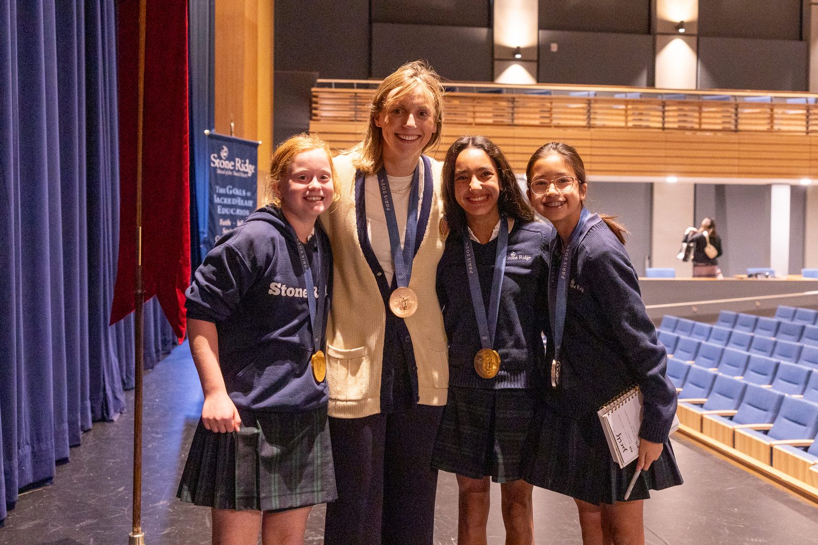 After Olympic champion swimmer Katie Ledecky spoke to Middle School students during her visit to her alma mater, Stone Ridge School of the Sacred Heart in Bethesda, Maryland, on Oct. 22, 2024, she let some students wear her medals from the recent Summer Olympic Games in Paris. From left to right are student Hope Murphy, Ledecky, and students Darya Tamiz and Eliana Liu. At the Paris Olympics, Ledecky won two gold medals, a silver medal and a bronze medal. (Catholic Standard photo by Mihoko Owada)