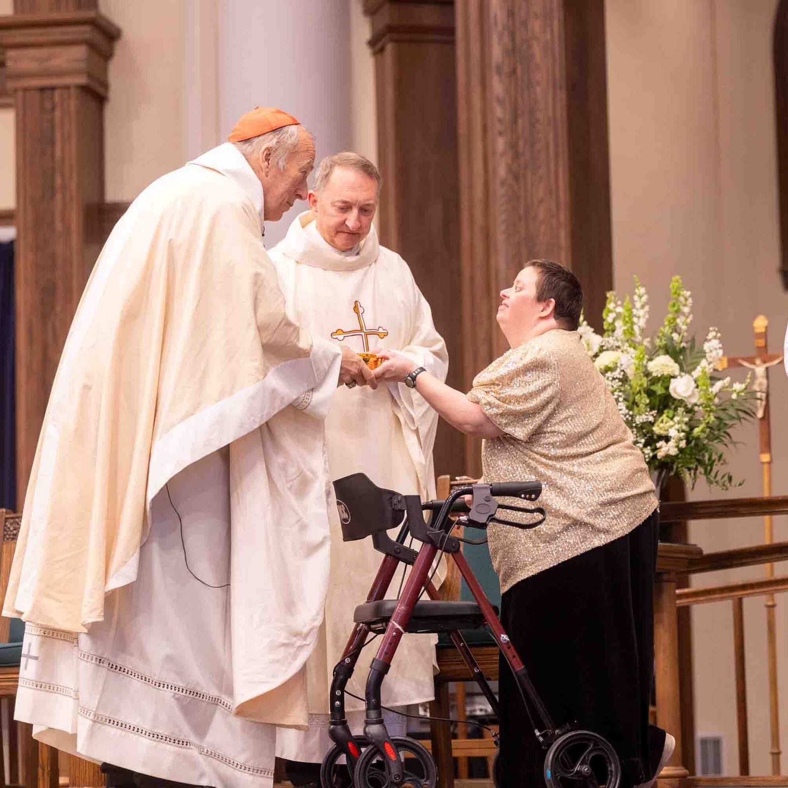 During the White Mass on Oct. 26, 2025 at Our Lady of Mercy Church in Potomac, Cardinal Robert W. McElroy receives an offertory gift from Cecelia Pauley, a member of Potomac Community Resources. Father Mark Knestout, at center, the pastor of Our Lady of Mercy, stands next to the cardinal. Potomac Community Resources, Inc. (PCR) is a private, nonprofit organization that promotes the participation of persons with intellectual and developmental disabilities in all aspects of community life. (Catholic Standard photo by Mihoko Owada)