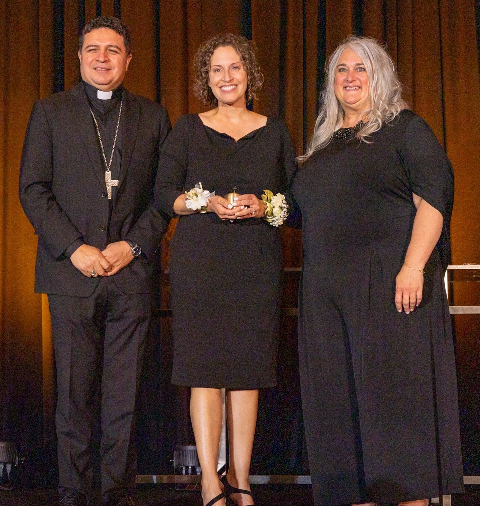 Just after receiving a golden apple signifying her Golden Apple Award, Ashley White, center, who teaches Spanish and religion at St. Mary’s School in Bryantown, stands with Washington Auxiliary Bishop Evelio Menjivar at left and Kelly Branaman, at right, the Secretary for Catholic Schools and Superintendent of Schools for The Roman Catholic Archdiocese of Washington. The 10 Golden Apple Award-winning teachers in the archdiocese were honored at a May 16 dinner at the Hotel at the University of Maryland in College Park. (Catholic Standard photo by Mihoko Owada)