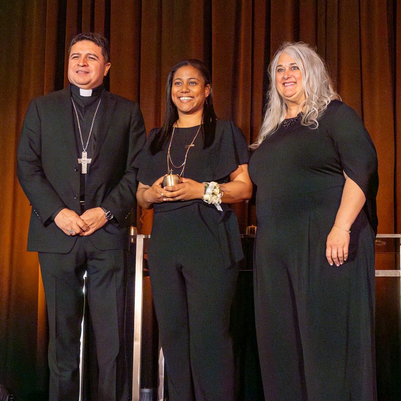 Just after receiving a golden apple signifying her Golden Apple Award, Renee Clark, center, who is a resource teacher at St. Mary of the Assumption School in Upper Marlboro, stands with Washington Auxiliary Bishop Evelio Menjivar at left and Kelly Branaman, at right, the Secretary for Catholic Schools and Superintendent of Schools for The Roman Catholic Archdiocese of Washington. The 10 Golden Apple Award-winning teachers in the archdiocese were honored at a May 16 dinner at the Hotel at the University of Maryland in College Park. (Catholic Standard photo by Mihoko Owada)