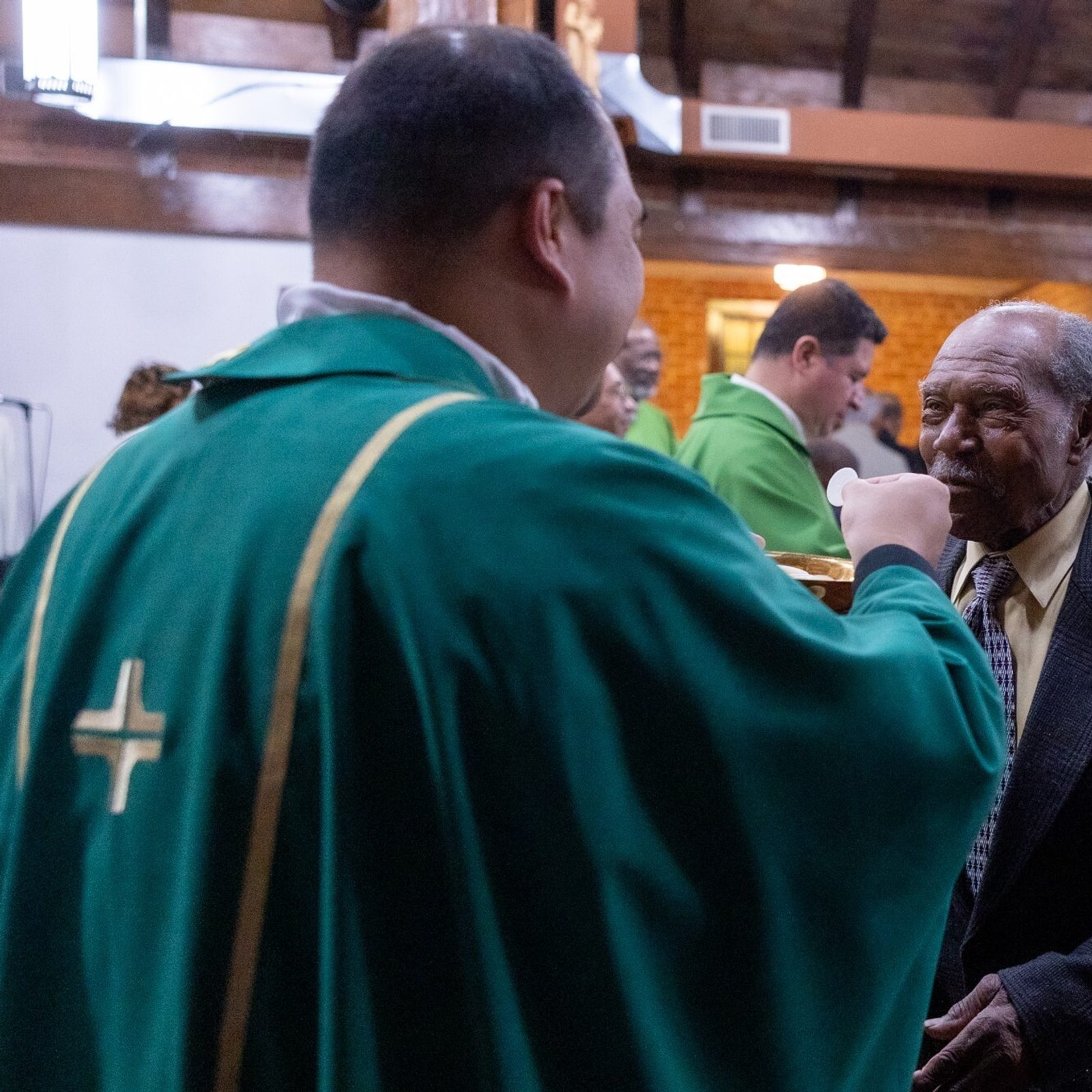 During a Nov. 16 Mass at St. Peter Claver Church in St. Inigoes, Maryland commemorating Black Catholic History Month, Father Patrick Agustin (at left) gives Communion to Ernest Hall, who has been the primary building maintenance and grounds contractor at St. Peter Claver Parish since the 1950s. He attended the now-closed St. Peter Claver School and the Cardinal Gibbons Institute at the parish. (Catholic Standard photo by Mihoko Owada)