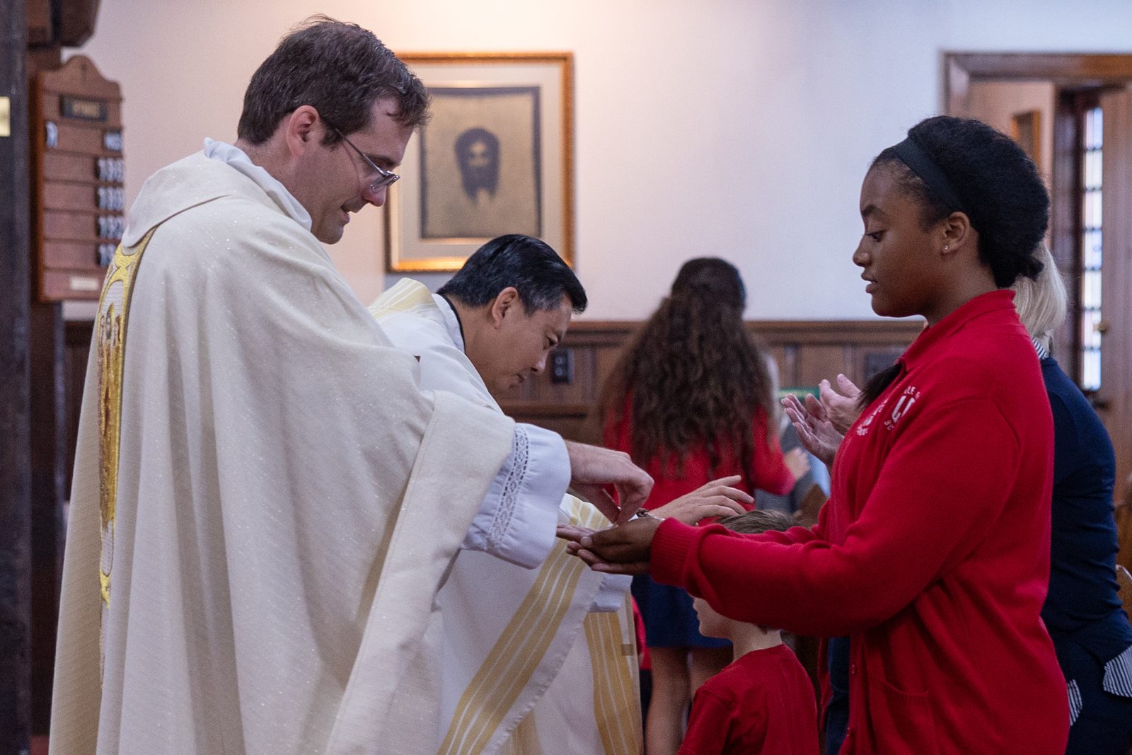 Kendall Pulliam, a student at Little Flower School in Great Mills, Maryland, receives Communion from Father Scott Holmer, the pastor of Holy Face Parish in Great Mills, during a Mass at Holy Face Church on Oct. 1, 2024 marking the feast day of the school’s patron saint, St. Thérѐse of Lisieux, who is known as the Little Flower. Blessing a child at the center is Father John Nguyen, the pastor of St. George Parish in Valley Lee who concelebrated the Mass. (Catholic Standard photo by Mihoko Owada)