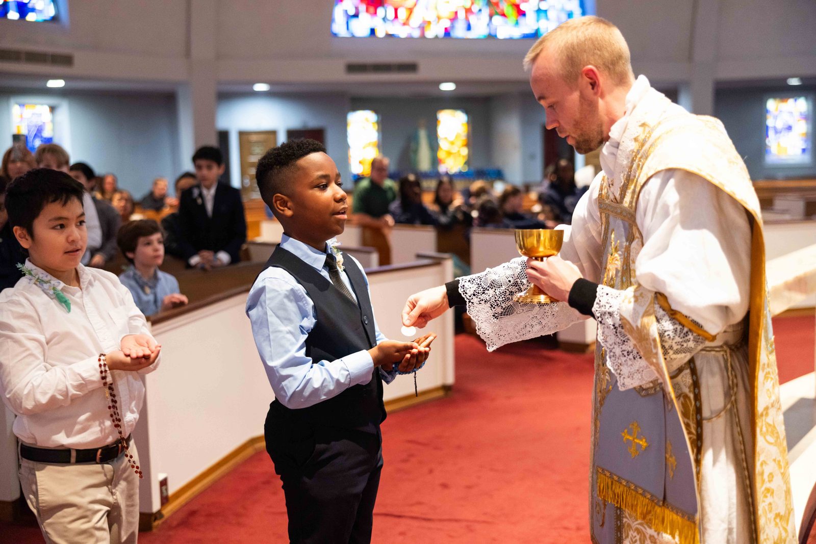 During a Mass on Jan. 31, 2025 at St. Mary’s Church in Rockville, Ariel Varela, an eighth grader at St. Mary’s School, receives his First Holy Communion from Father Nathanael Anderson, a parochial vicar at St. Mary’s who celebrated the Mass where 12 St. Mary’s students received their First Communion. At left is Christopher Tran, a fifth grader about to receive his First Communion. (Catholic Standard photo by Andrew Biraj)