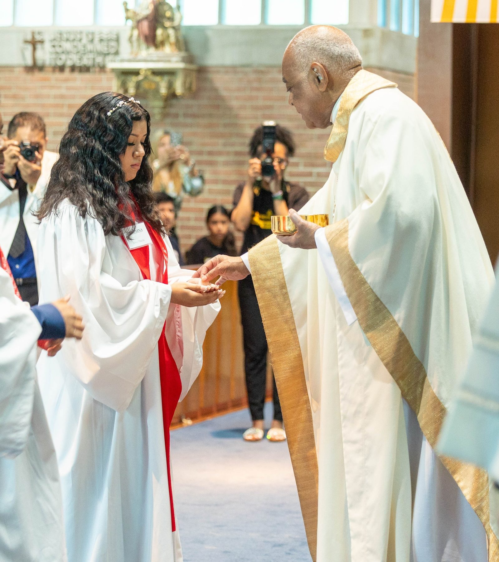 Ashley Pineda, a member of the class of 2027 at Don Bosco Cristo Rey High School in Takoma Park, receives her First Holy Communion from Cardinal Wilton Gregory at a May 24 Mass at Our Lady of Sorrows Church. (Catholic Standard photo by Mihoko Owada)