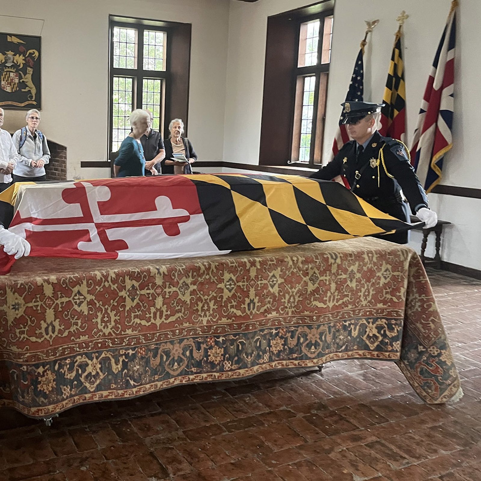 Before a reinterment ceremony for the remains of eight young children from colonial-era Maryland being brought back to the site of the rebuilt 1667 Brick Chapel in Historic St. Mary’s City on Sept. 20, 2025, Corporal Benjamin Luffey and Deputy Jordan Wagner of the St. Mary’s County Sheriff’s Office place the Maryland flag on the pine coffin bearing the remains. The procession for the ceremony began at the reconstructed State House of 1676 located about one-half mile from the Brick Chapel. (Catholic Standard photo by Mark Zimmerman)