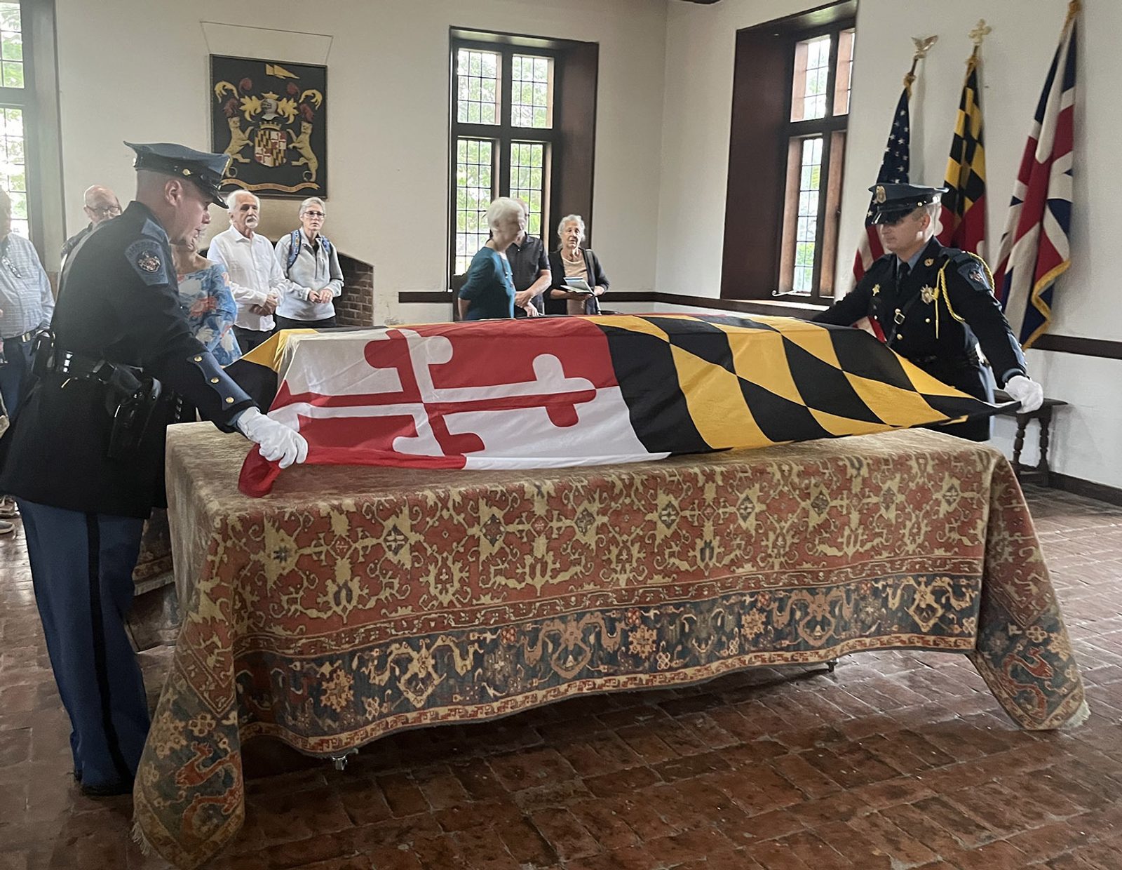 Before a reinterment ceremony for the remains of eight young children from colonial-era Maryland being brought back to the site of the rebuilt 1667 Brick Chapel in Historic St. Mary’s City on Sept. 20, 2025, Corporal Benjamin Luffey and Deputy Jordan Wagner of the St. Mary’s County Sheriff’s Office place the Maryland flag on the pine coffin bearing the remains. The procession for the ceremony began at the reconstructed State House of 1676 located about one-half mile from the Brick Chapel. (Catholic Standard photo by Mark Zimmerman)