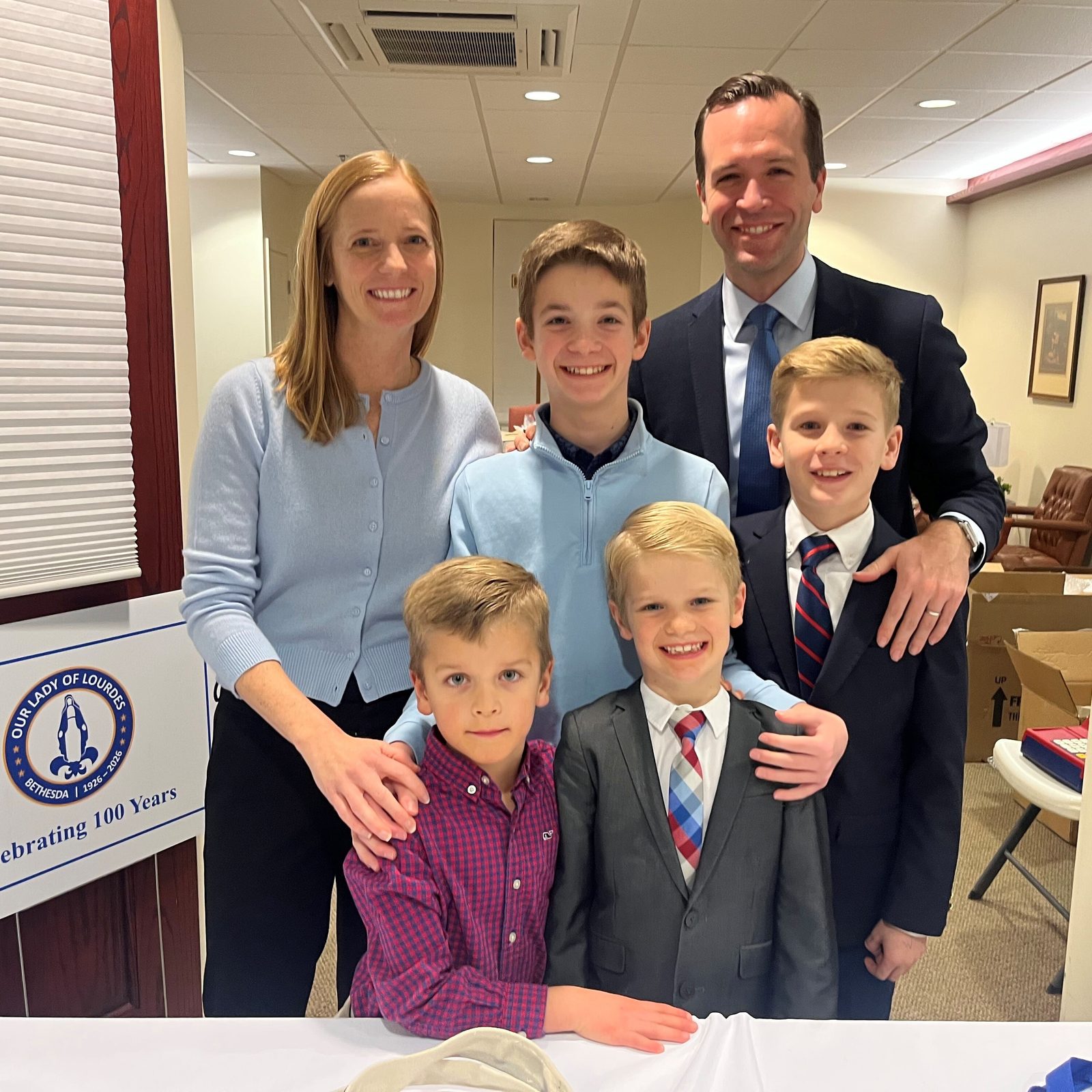 Before a Feb. 11 Mass at Our Lady of Lourdes Church in Bethesda marking the parish’s 100th anniversary, parishioners Jim and Jill Gadwood pose for a photo with their sons Gregory, Mark, Henry and Peter, who are students at Our Lady of Lourdes School. Jim and Jill Gadwood are part of the parish’s 100th anniversary committee and were selling souvenirs commemorating the milestone. (Catholic Standard photo by Mark Zimmermann)