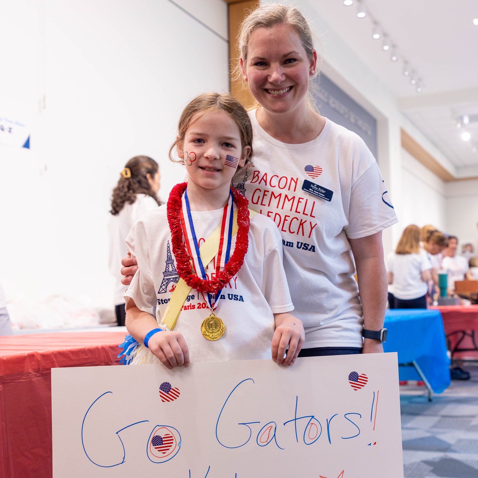 Before a July 25 pep rally at Stone Ridge School of the Sacred Heart in Bethesda, rising fourth grader Evie Kalas holds a poster cheering on three of the school’s graduates – Katie Ledecky (class of 2015), Phoebe Bacon (class of 2020) and Erin Gemmell (class of 2023) – who are members of the U.S. Olympic Swimming Team competing in the Summer Olympics in Paris. She is joined by her mother Kate Kalas, Stone Ridge’s director of marketing and communications. (Catholic Standard photo by Mihoko Owada)