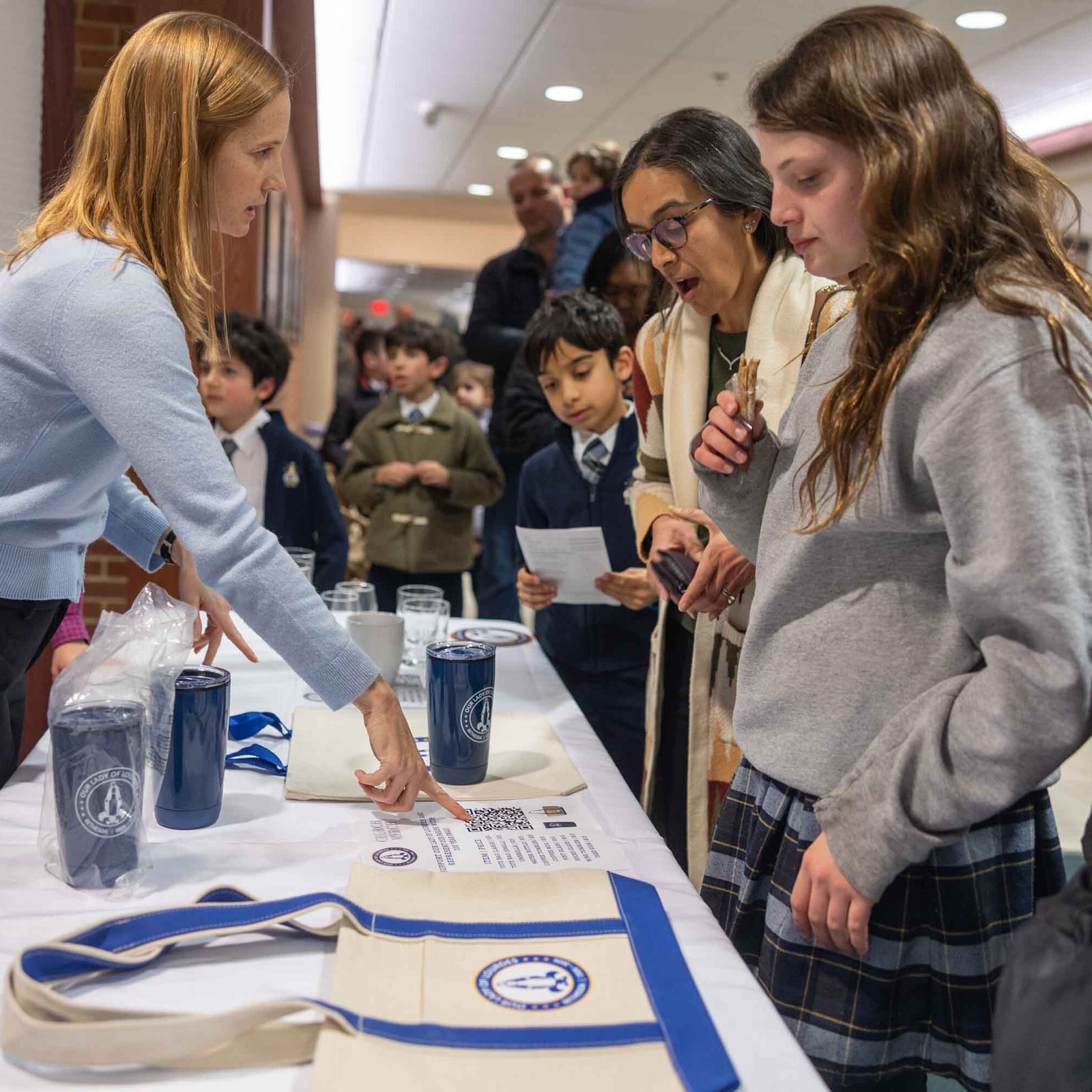After a 100th anniversary Mass for Our Lady of Lourdes Parish in Bethesda on Feb. 11, parishioner Jill Gadwood, a member of the 100th anniversary committee, volunteers at a table where commemorative items were for sale. The guests at right included Our Lady of Lourdes students Maisey Looney (wearing a gray sweatshirt) and Devan Katyal (holding a program). (Catholic Standard photo by Mihoko Owada)