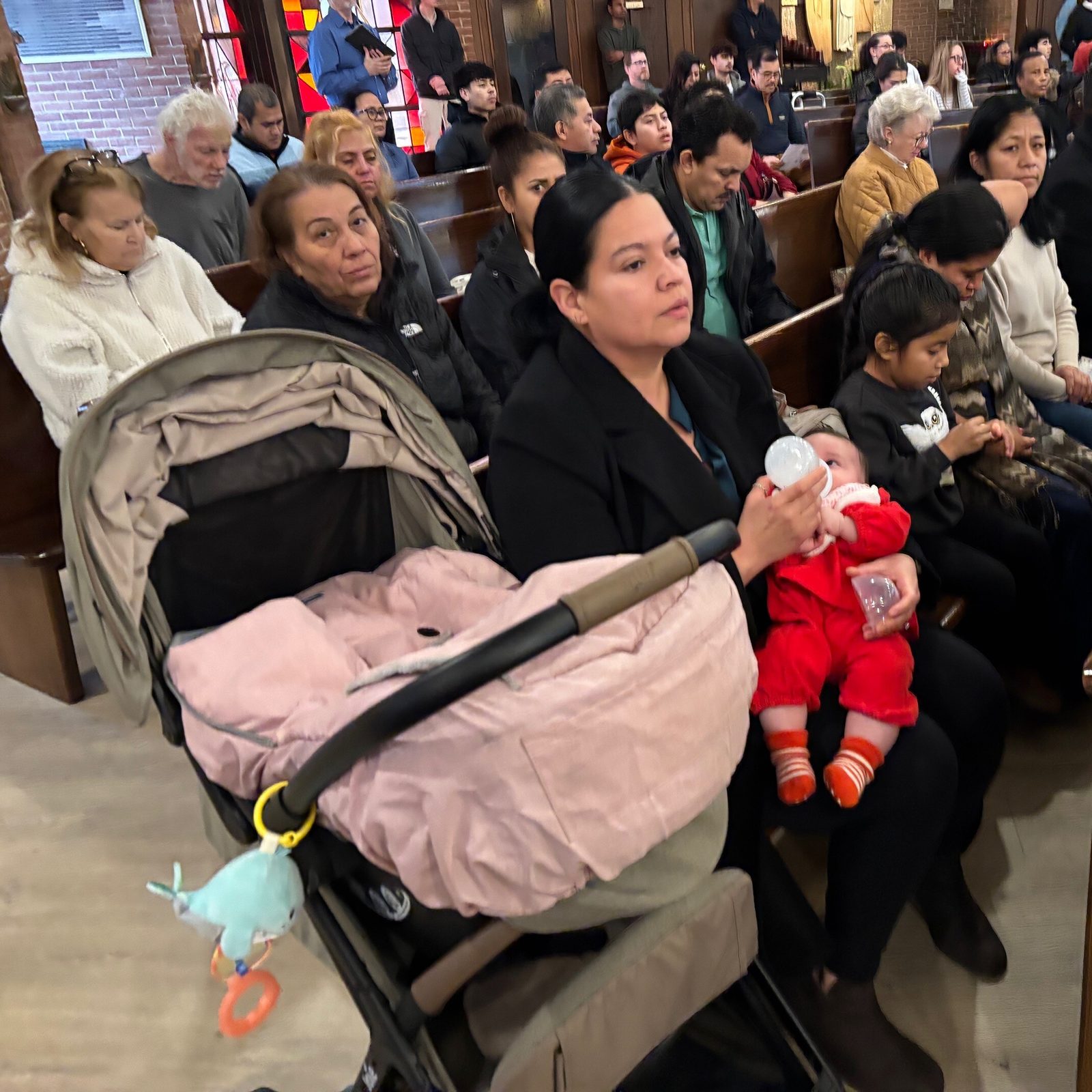 Madre de familia alimenta a su pequeña hija mientras escucha atenta la homilía del cardenal Robert McElroy, durante la ﻿la misa anual en conmemoración del legado del reverendo Martin Luther King Jr. celebrada en la parroquia San Judas Tadeo en Rockville, Maryland, el 18 de enero de 2026﻿.