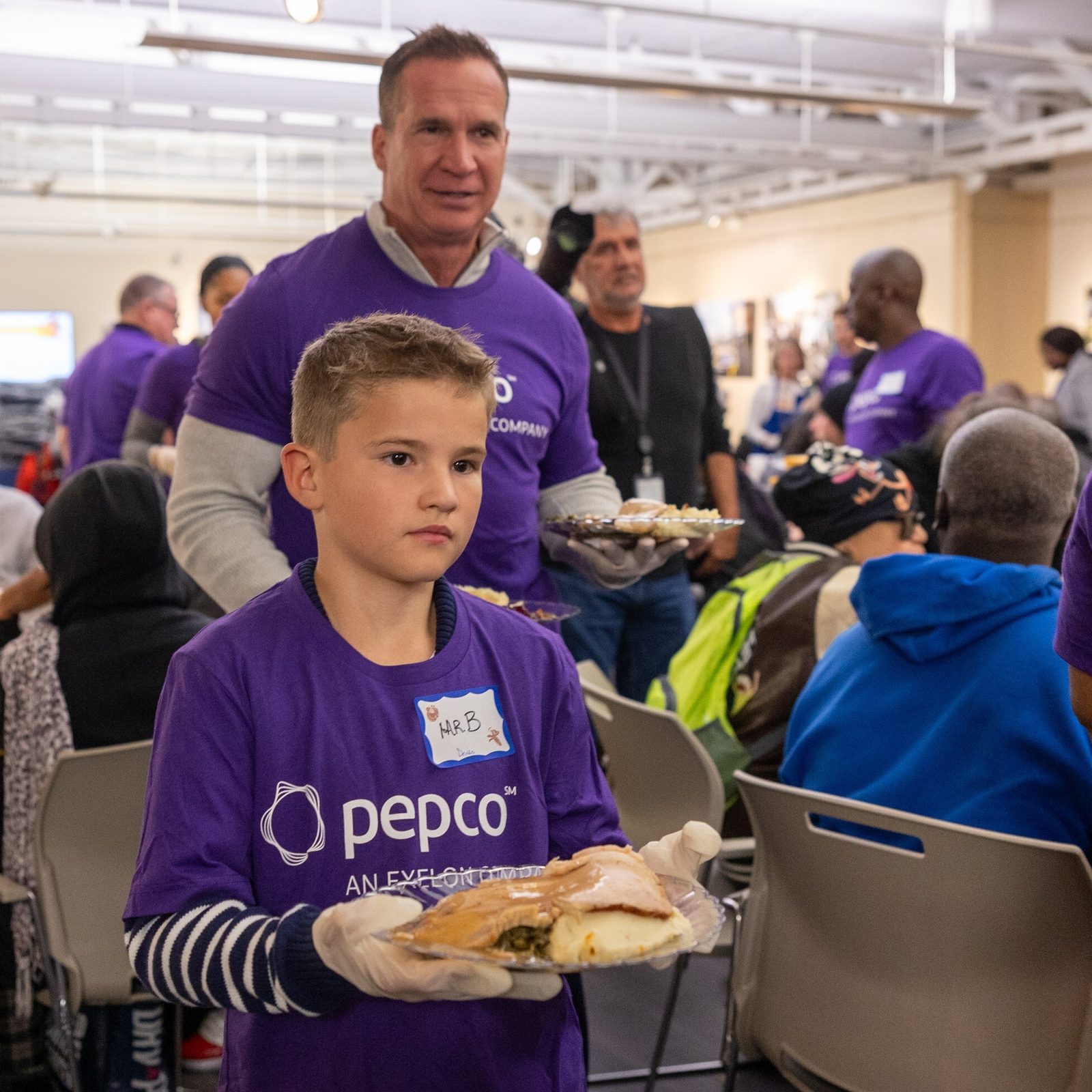 In the photo above, Tyler Anthony, the president and CEO of Pepco Holdings, is joined by his 8-year-old son Blake in serving meals to guests at the Nov. 26 Thanksgiving dinner given through Catholic Charities’ St. Maria’s Meals program and hosted by Pepco at its Edison Place Gallery in downtown Washington, D.C. In the photo below, Blake Anthony serves a meal to a guest at the Thanksgiving dinner. (Catholic Standard photos by Mihoko Owada)