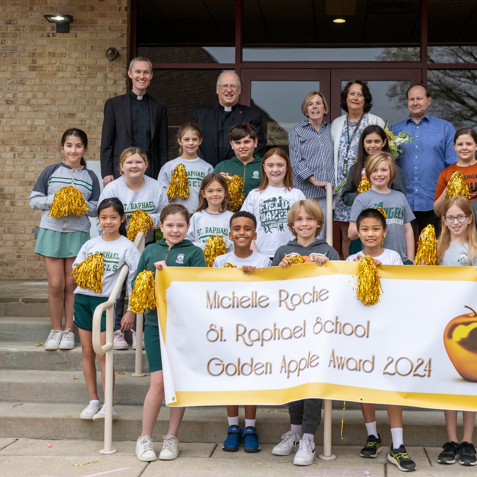 La maestra Michelle Roche y sus alumnos de la escuela St. Raphael en Rockville (MD) posan luego de enterarse que había ganado el premio Golden Apple 2024. (Detrás de ellos, de izq. a der.) Los sacerdotes Christian Huebner y Michael Salah, párroco de San Rafael; Teri Dwyer, directora de la escuela; y Michelle Roche y su esposo, Bill Roche. Foto/ Mihoko Owada