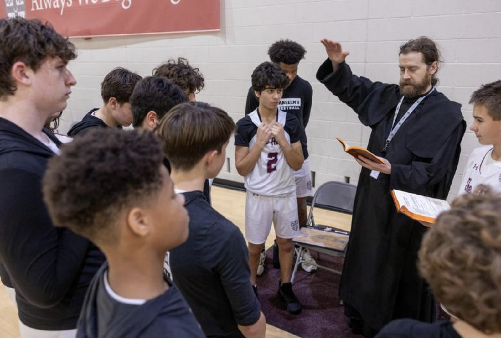 Benedictine Father Samuel Springuel prays with the JV basketball team of 9th and 10th graders from St. Anselm's Abbey School in Washington in the school gym before the game. (Catholic Standard photo by Mihoko Owada)