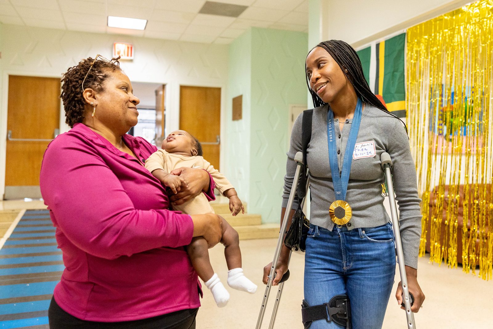 During a Sept. 10 pizza party for residents and staff at St. Ann’s Center for Children, Youth and Families in Hyattsville, staff member Nichelle Lucas and a young resident meet Thea LaFond-Gadson, who won a gold medal in the women’s triple jump competition at the recent Summer Olympics in Paris. (Catholic Standard photo by Mihoko Owada)