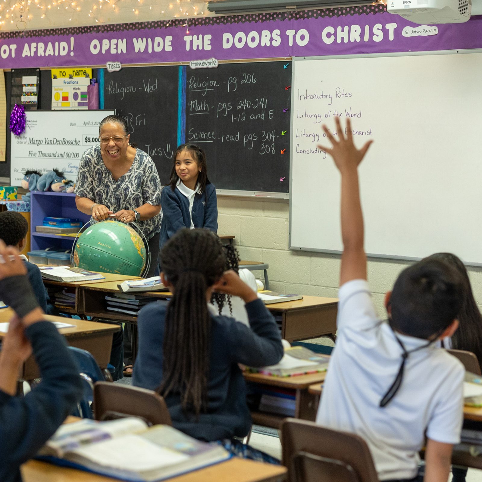 Shortly after the surprise announcement on April 15 that she is a 2024 Golden Apple Award winning teacher for The Roman Catholic Archdiocese of Washington, Margo VanDenBossche returned to her third grade classroom at Saint Peter’s School in Waldorf. Standing next to her is third grader Enira Garcia. (Catholic Standard photo by Mihoko Owada)