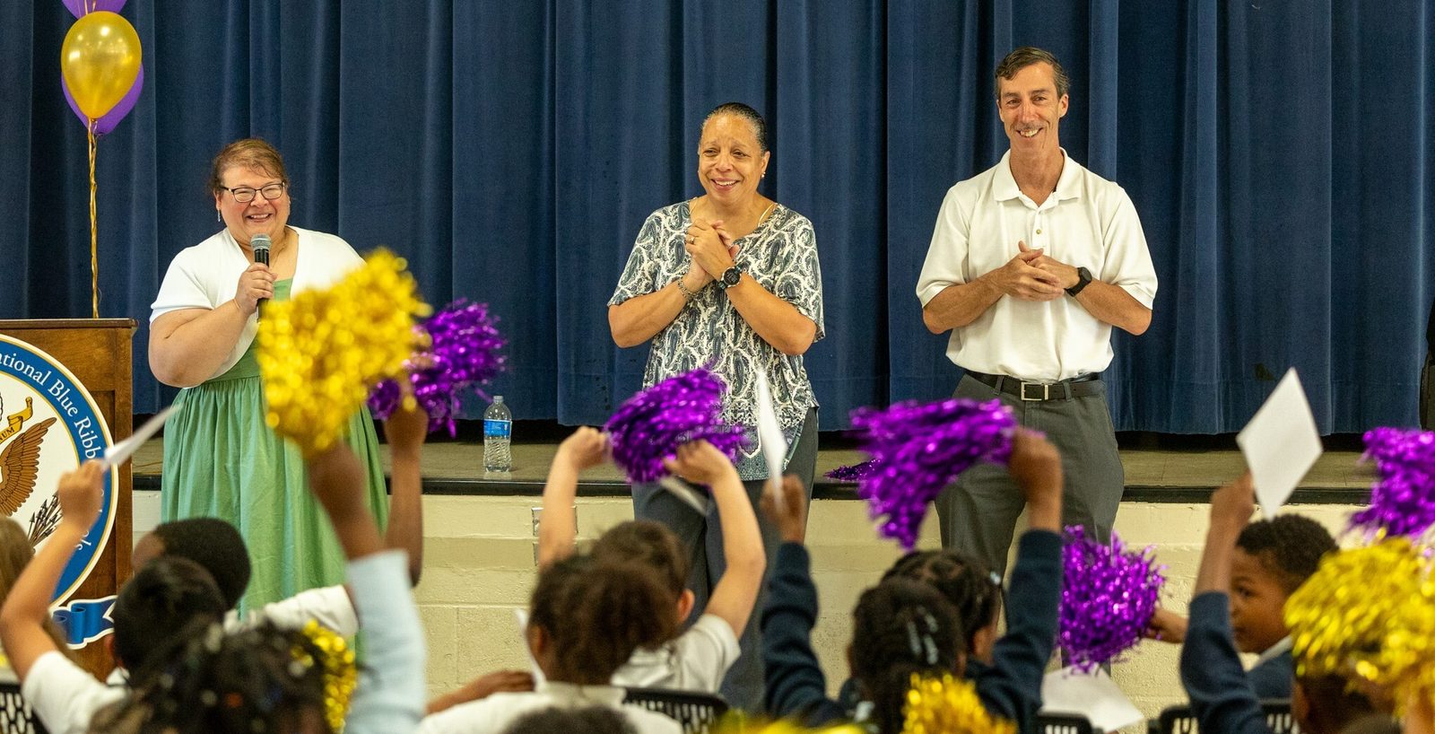 At center, Margo VanDenBossche, a third grade teacher at Saint Peter’s School in Waldorf, Maryland, has tears of joy after it was announced on April 15 that she is a 2024 Golden Apple Award winning teacher. At right is her husband Chuck VanDenBossche, and at left is Christina Mendez-Hall, the assistant superintendent for Catholic identity and accreditation in the Catholic Schools Office of The Roman Catholic Archdiocese of Washington, who made the announcement. (Catholic Standard photo by Mihoko Owada)