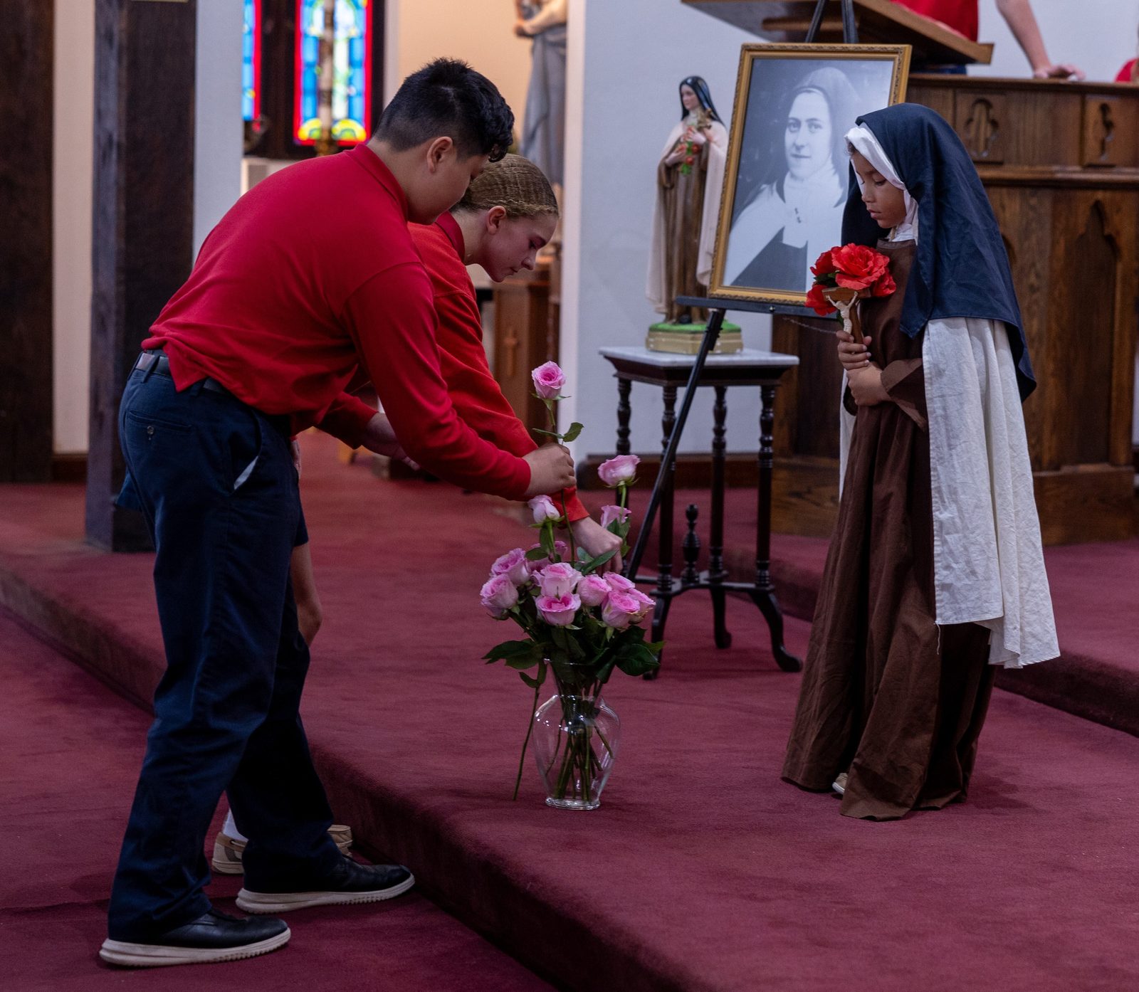 Zachary Phan and Dakota Hancock, who are seventh graders at Little Flower School in Great Mills, Maryland, put roses in a vase during a Mass on Oct. 1, 2024 at Holy Face Church in Great Mills for the feast day of the school’s patron saint, St. Thérѐse of Lisieux, who is known as the Little Flower. At right, Charlotte Hartzer, a fourth grader at Little Flower School, portrays St. Thérѐse at the Mass. (Catholic Standard photo by Mihoko Owada)