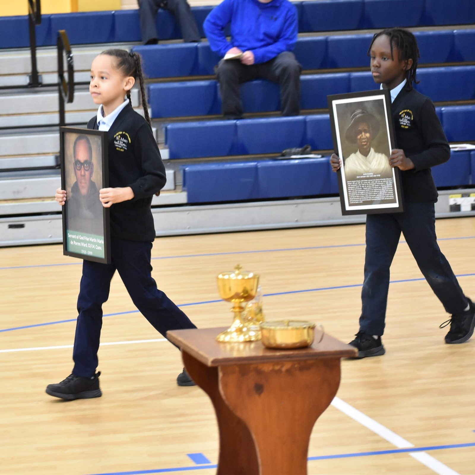 During a Mass for Black History Month on Feb. 6 at St. Mary of the Assumption Catholic School in Upper Marlboro, second graders Emma Howard and Lion George carry portraits of two of the “sacred seven,” the Black Catholics being considered for sainthood – Servant of God Friar Martin Maria de Porres Ward and Servant of God Julie Greeley. (Photo by Michelle Dunn from St. Mary of the Assumption Catholic School)