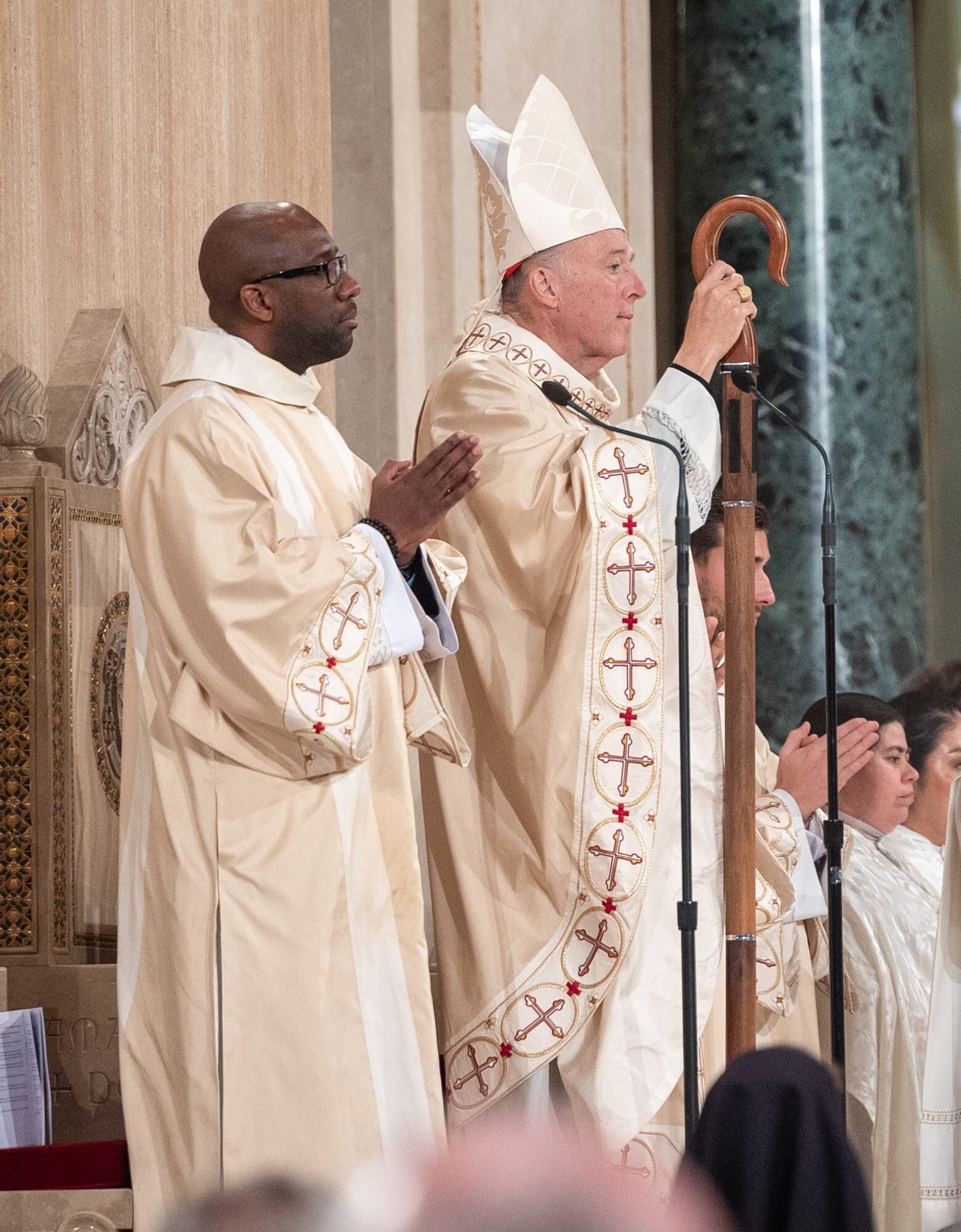 Cardinal Robert McElroy, at right, holds his crozier as he stands during his Solemn Mass of Installation as the new archbishop of Washington on March 11, 2025 at the Basilica of the National Shrine of the Immaculate Conception. At left is Deacon Yannick Allepot, who assisted at the Mass. (Catholic Standard photo by Mihoko Owada)