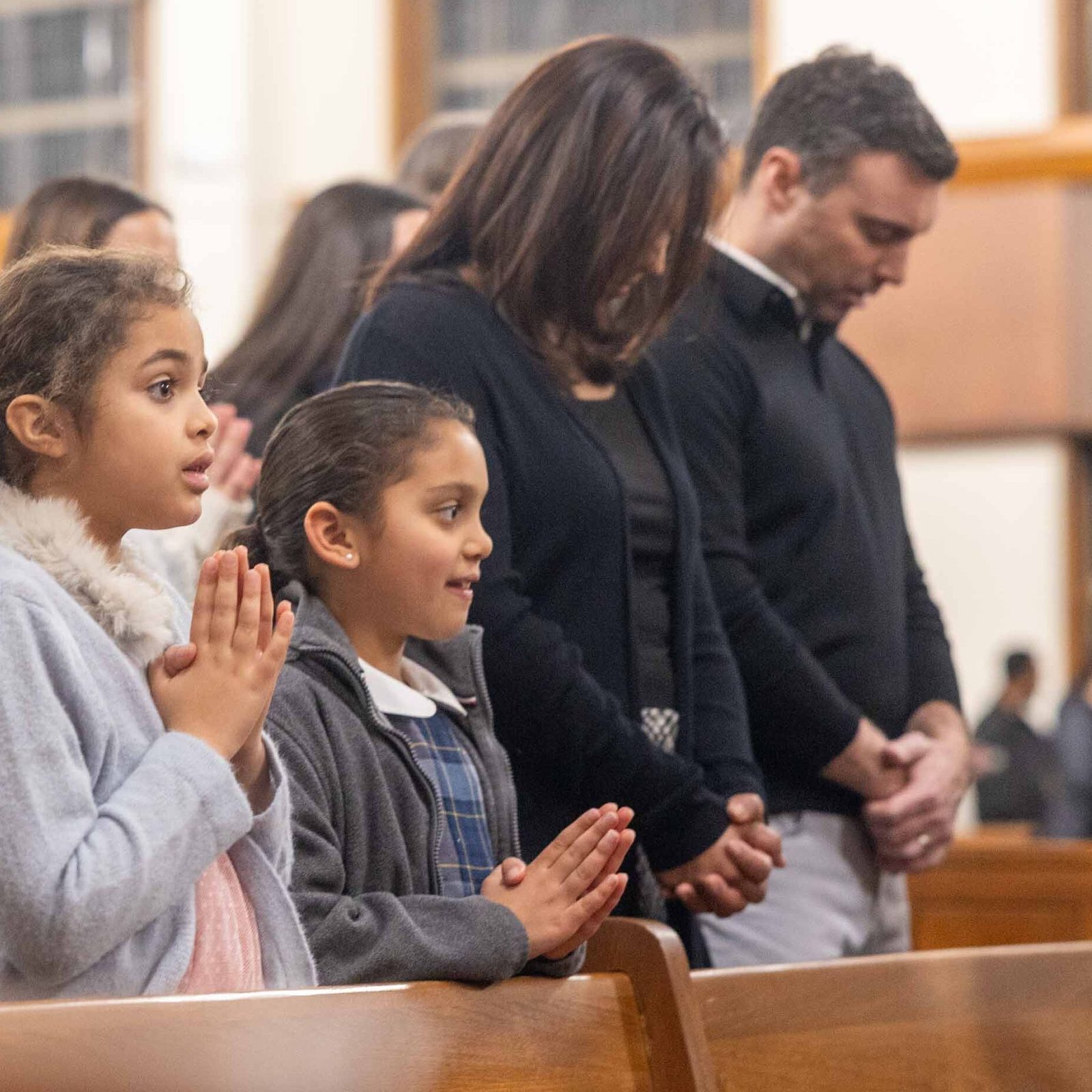 During a Feb. 11 Mass at Our Lady of Lourdes Church in Bethesda marking the parish’s 100th anniversary, Margot Dickerson (at left), prays beside fellow Our Lady of Lourdes student Maggie Cannito and her parents, Gregory and Nicole Cannito. (Catholic Standard photo by Mihoko Owada)