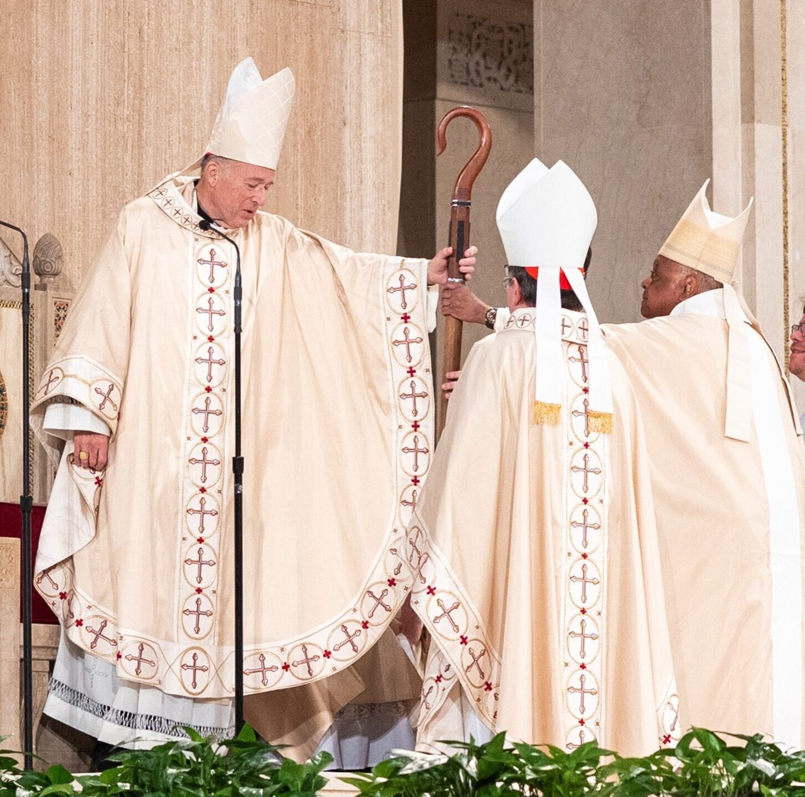 Cardinal Robert McElroy (at left), the newly installed archbishop of Washington, is handed the crozier – the shepherd’s staff symbolic of his office – by Cardinal Wilton Gregory (at right), the archbishop emeritus of Washington, during the Solemn Mass of Installation on March 11, 2025 at the Basilica of the National Shrine of the Immaculate Conception. Standing at the center is Cardinal Christophe Pierre, the apostolic nuncio to the United States who moments earlier read the apostolic mandate from Pope Francis appointing Cardinal McElroy as the archbishop of Washington. (Catholic Standard photo by Mihoko Owada)