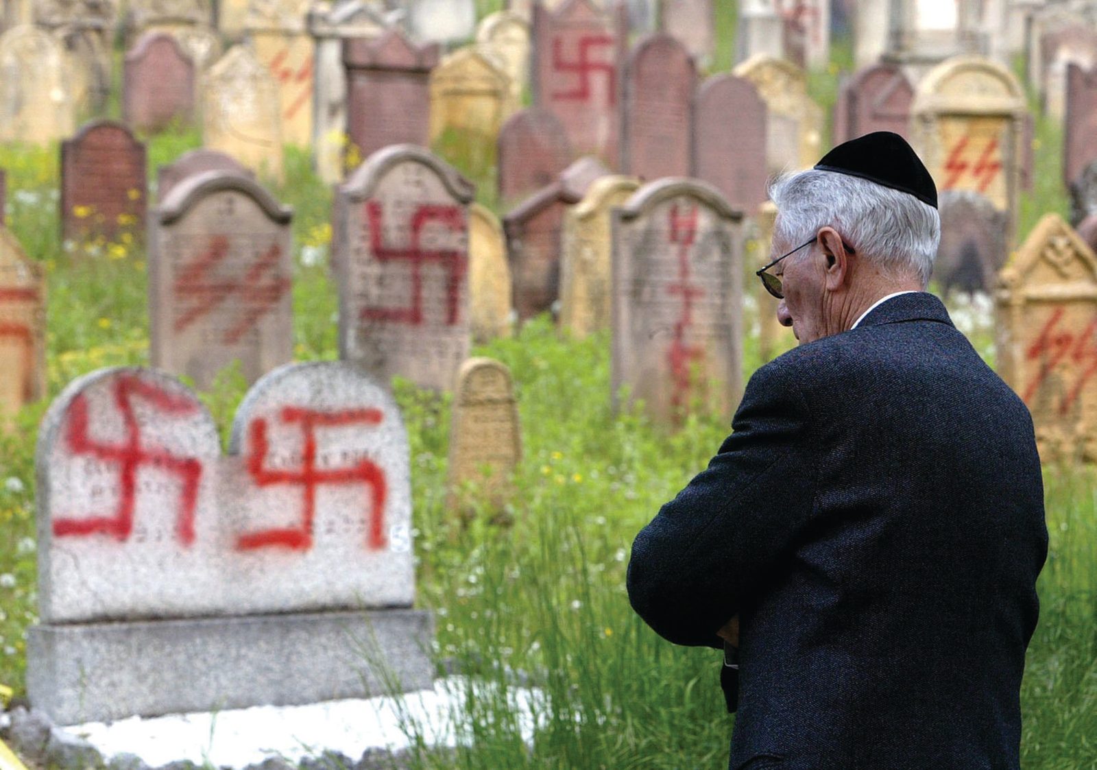 In this file photo, a member of the Jewish community views anti-Semitic graffiti on tombstones at the Jewish cemetery in Herrlisheim, France, where several graves were desecrated with swastikas and slogans written in German, and experts indicated the trend was increasing. (CNS photo from Reuters)