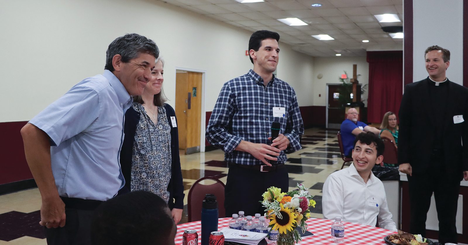 Seminarian Sam Guevara (at center) speaks at the July 27 Seminarian Family Day luncheon at St. Mary’s Parish in Landover Hills, Maryland. At left are his parents with his parents, Nick and Jean Guevara. Seated at right is seminarian Julian Jimenez. The luncheon and the Mass preceding it were sponsored by The Roman Catholic Archdiocese of Washington. Standing at right is Father Mark Ivany, the archdiocese’s director of priest vocations. (Catholic Standard photo by Javier Diaz)