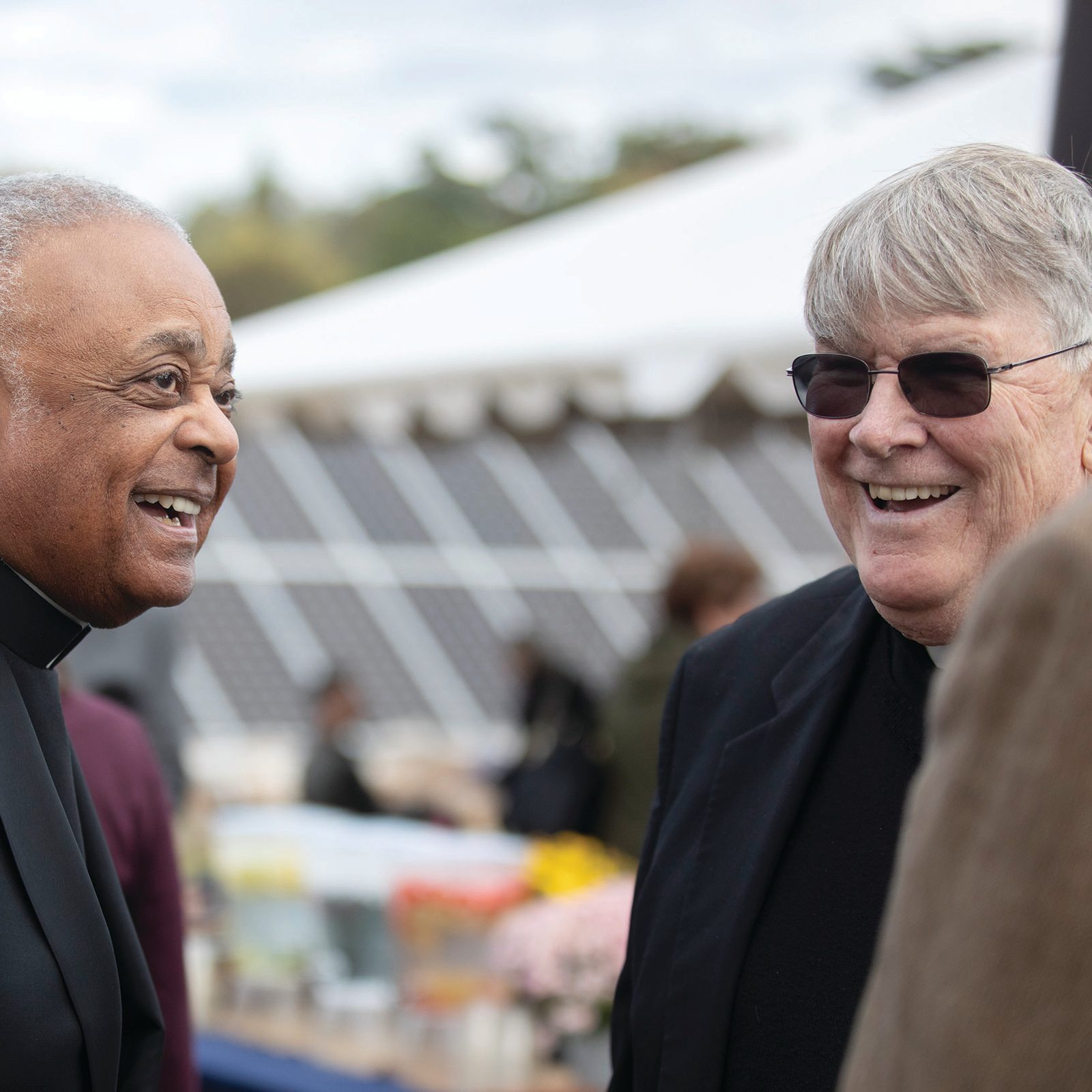 Then-Archbishop Wilton Gregory of Washington and Msgr. John Enzler, the president and CEO of Catholic Charities of the Archdiocese of Washington, share a laugh before the Oct. 17, 2019 blessing of the solar array on property owned by Catholic Charities that is being leased to produce renewable energy for residents of Washington, D.C. Behind them can be seen some of the more than 5,000 ground-mounted solar panels that are now generating energy there. (Catholic Standard photo by Andrew Biraj)