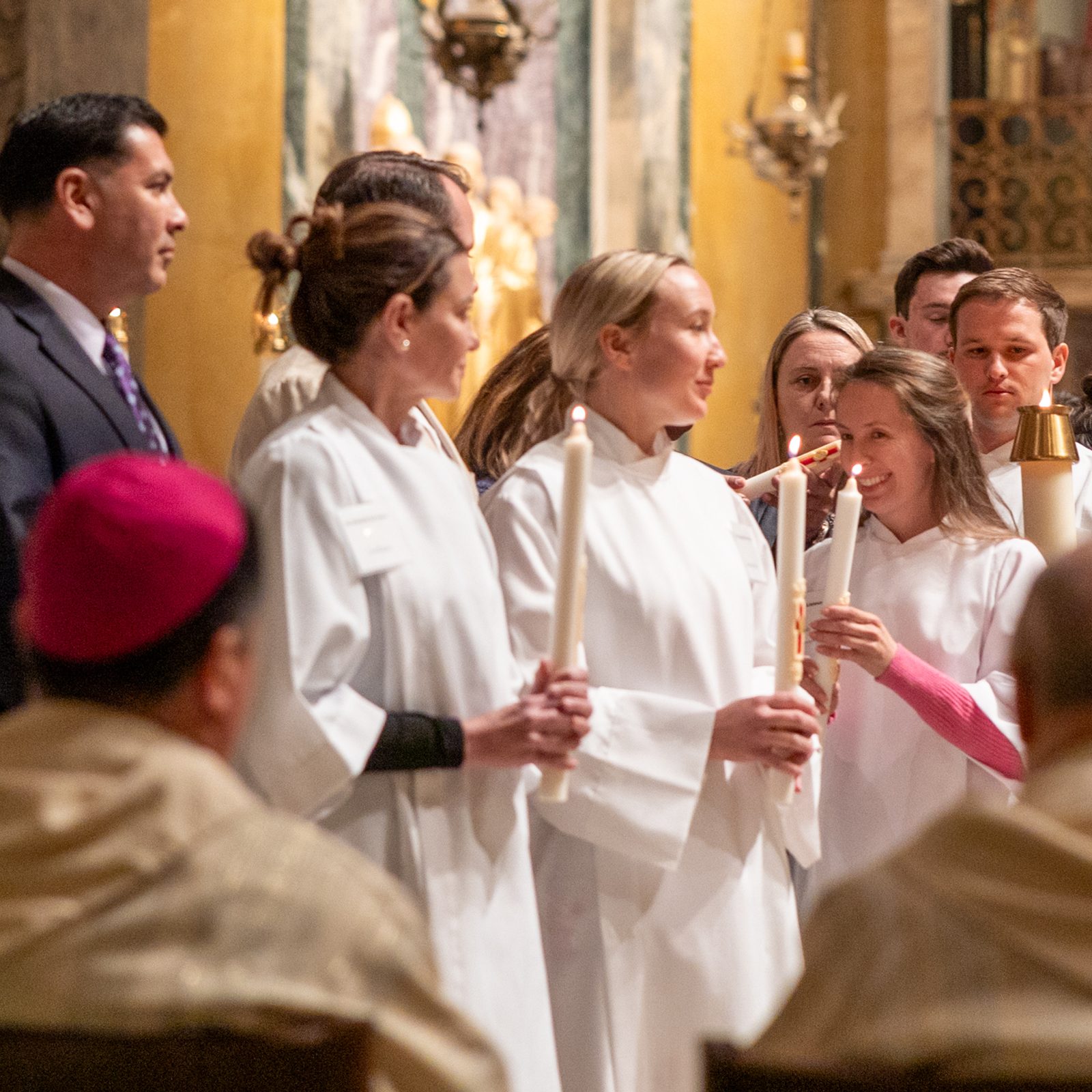 People newly baptized at St. Matthew’s Cathedral in Washington during the March 30 Easter Vigil stand together near the altar, holding candles and wearing their baptismal garments. (Catholic Standard photo by Mihoko Owada)