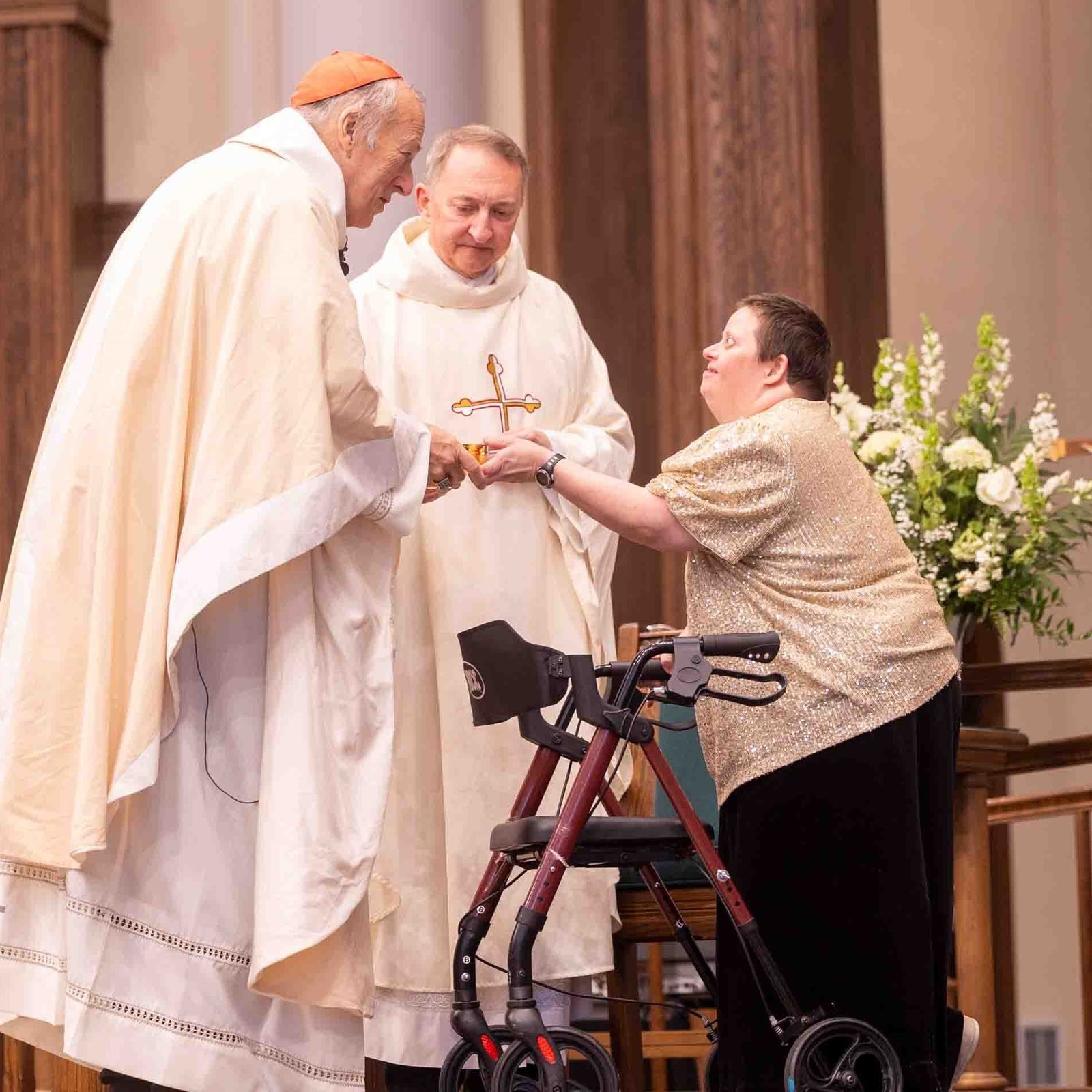 During the White Mass on Oct. 26, 2025 at Our Lady of Mercy Church in Potomac, Cardinal Robert W. McElroy receives an offertory gift from Cecelia Pauley, a member of Potomac Community Resources. Father Mark Knestout, at center, the pastor of Our Lady of Mercy, stands next to the cardinal. Potomac Community Resources, Inc. (PCR) is a private, nonprofit organization that promotes the participation of persons with intellectual and developmental disabilities in all aspects of community life. (Catholic Standard photo by Mihoko Owada)