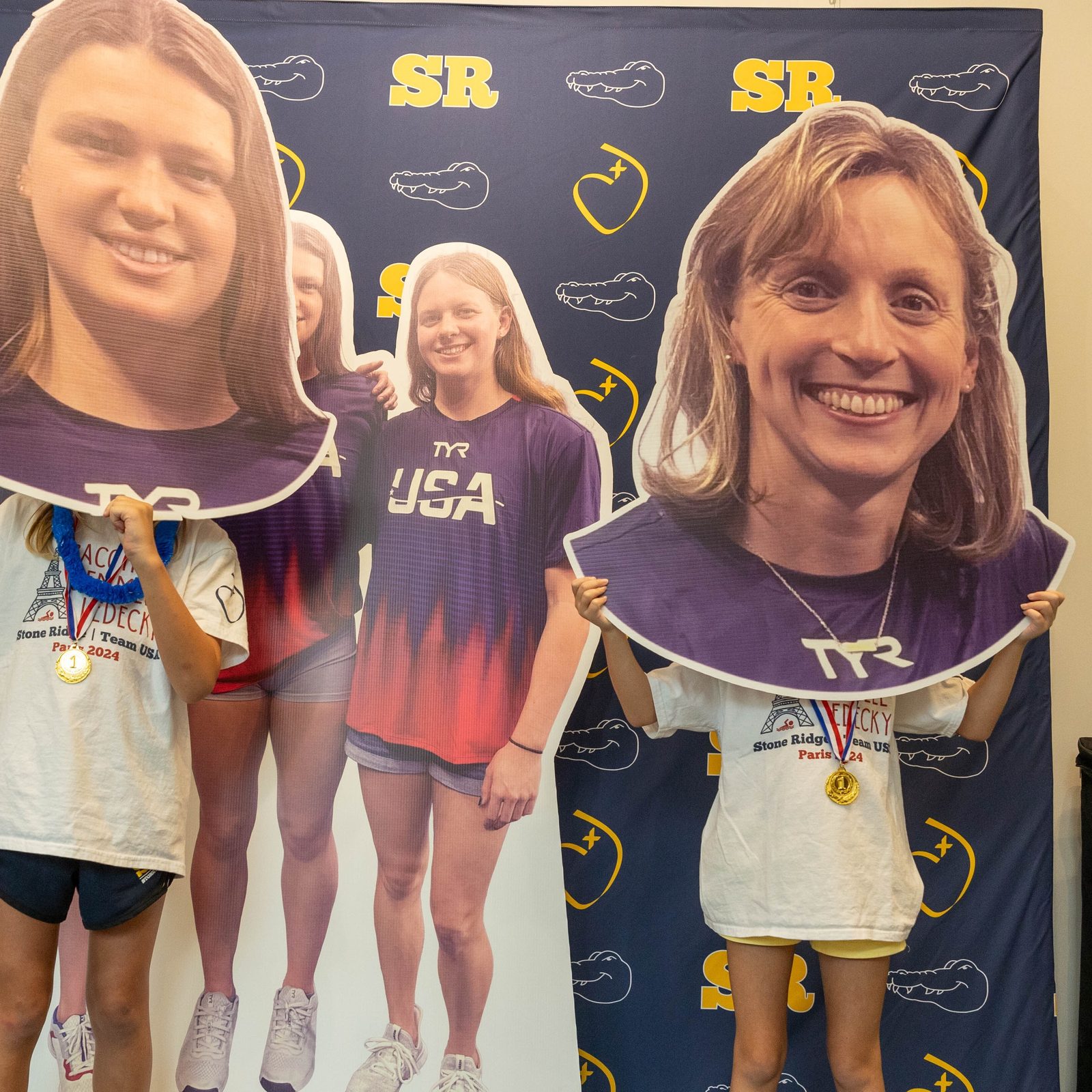 Students pose holding large cutout portraits of Stone Ridge graduates Phoebe Bacon and Katie Ledecky, who are swimming in the Paris Olympics, along with fellow alumnae Erin Gemmell, seen in the poster in the background. (Catholic Standard photo by Mihoko Owada)