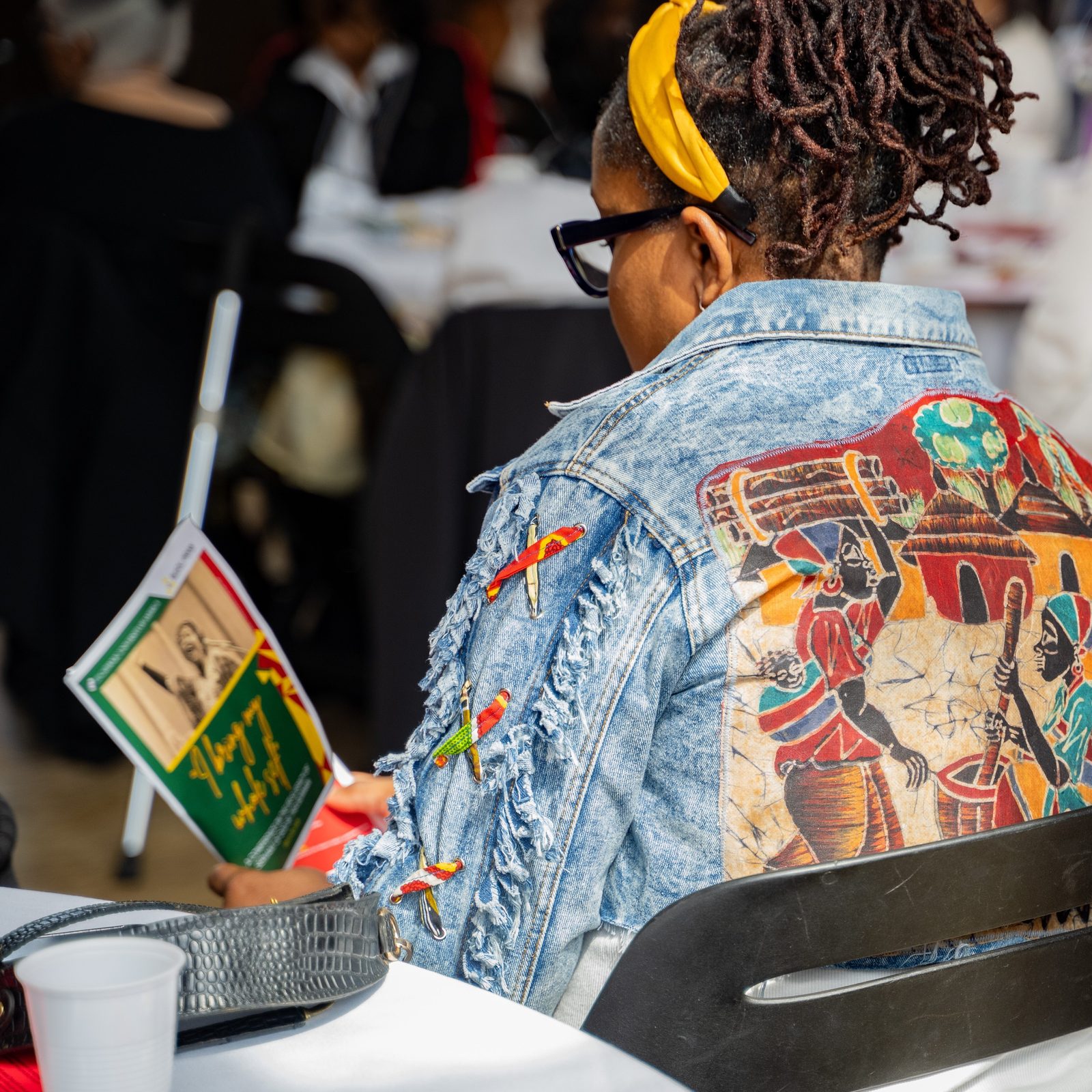 An attendee wearing a denim jacket featuring an African village scene looks through a program during a March 29 conference at The Catholic University of America honoring the life and legacy of Sister Thea Bowman, one of seven U.S. Black Catholics being considered for sainthood. (Catholic Standard photo by Nicole Olea)
