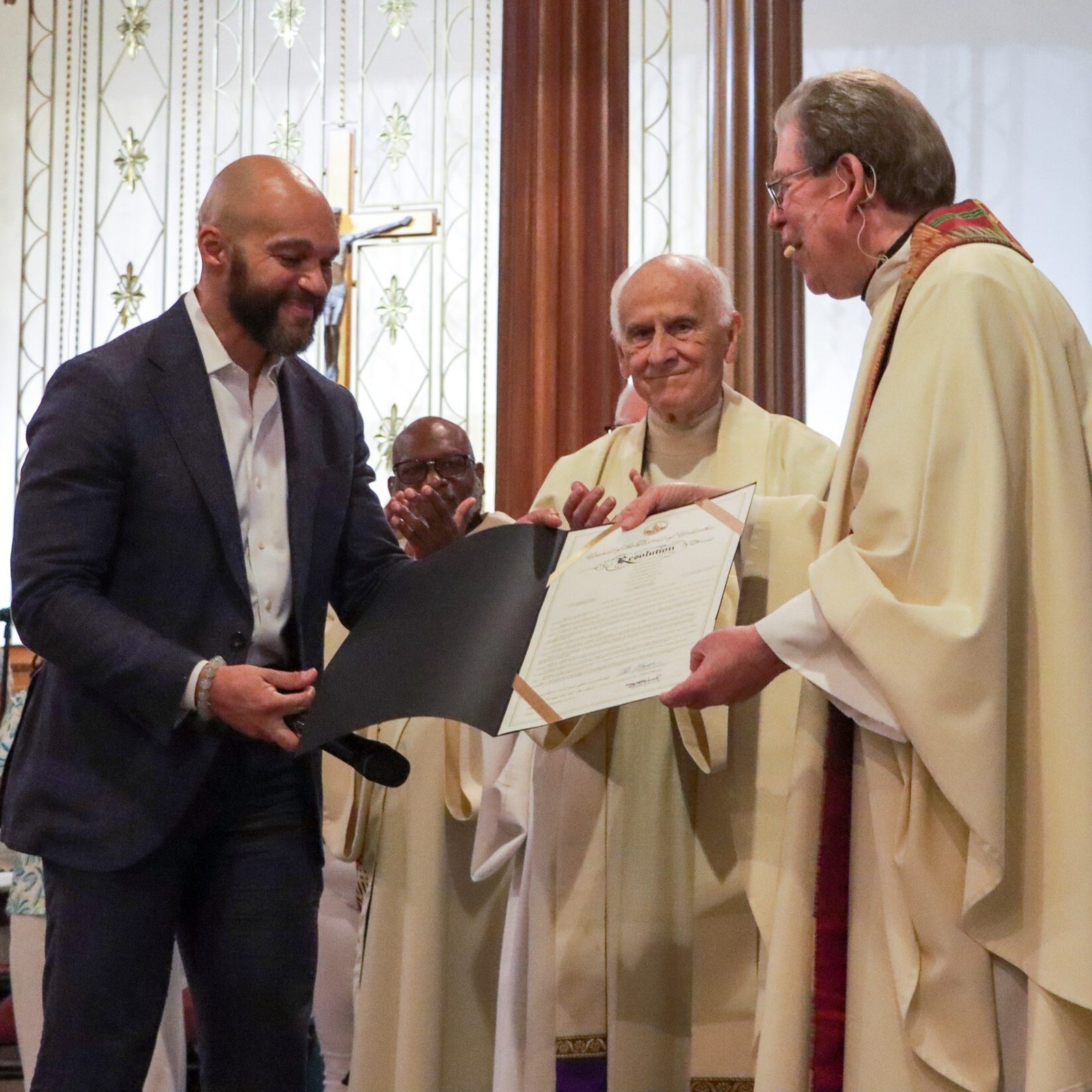 Robert C. White Jr., an At-Large Councilmember of the Council of the District of Columbia, presents Father Michael Kelley with a proclamation from the council honoring the priest for his longtime service as pastor of St. Martin of Tours Parish in Washington, D.C. The presentation came during a Mass that Father Kelley celebrated at St. Martin’s Catholic Church on May 18, 2025 marking his 50th anniversary as a priest. Father Kelley has served as St. Martin’s pastor for the past 33 years. Councilmember White and his wife Christy and their daughters Madison and Monroe are St. Martin’s parishioners, and the councilmember’s father, Deacon Bobby White, serves at the parish. Councilmember White also sings in St. Martin’s Gospel Choir. Standing at center is Father Michael Bryant, a priest mentor to Father Kelley who was a concelebrant at the Mass along with Father John Mudd, another mentor to him. (Catholic Standard photo by Javier Diaz)